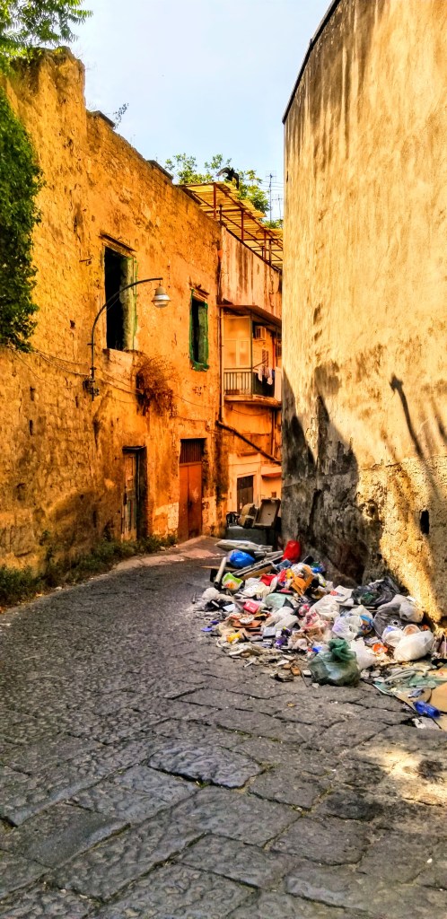 A pile of garbage at the side of a narrow street in Naples, Italy.