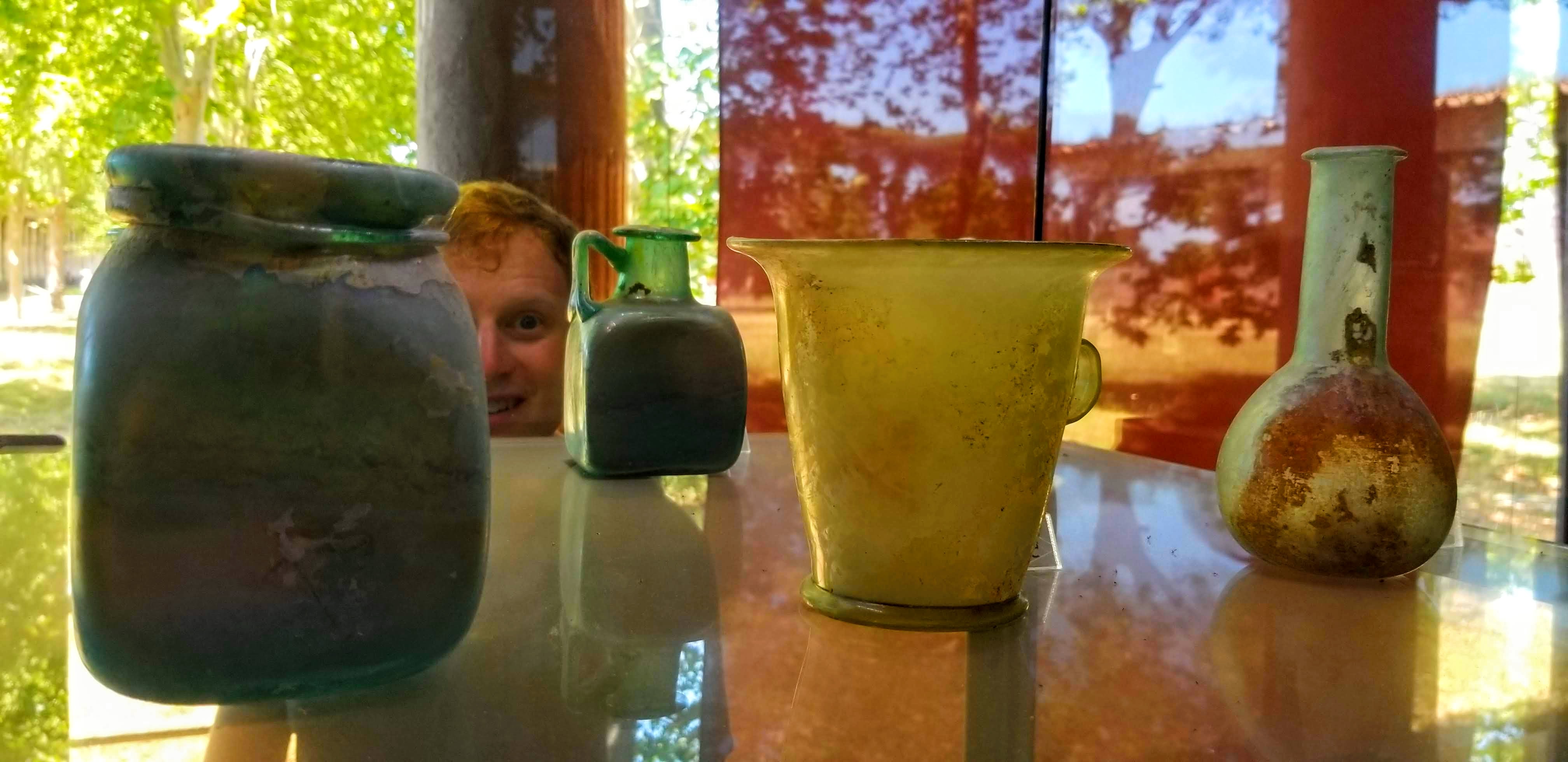 A man's face peers between ancient Roman glass bottles at Pompeii.
