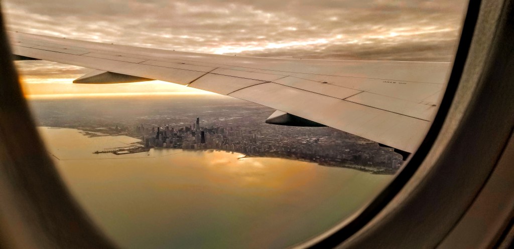 View of Chicago skyline out of an airplane window, airplane wing cutting across the sky.