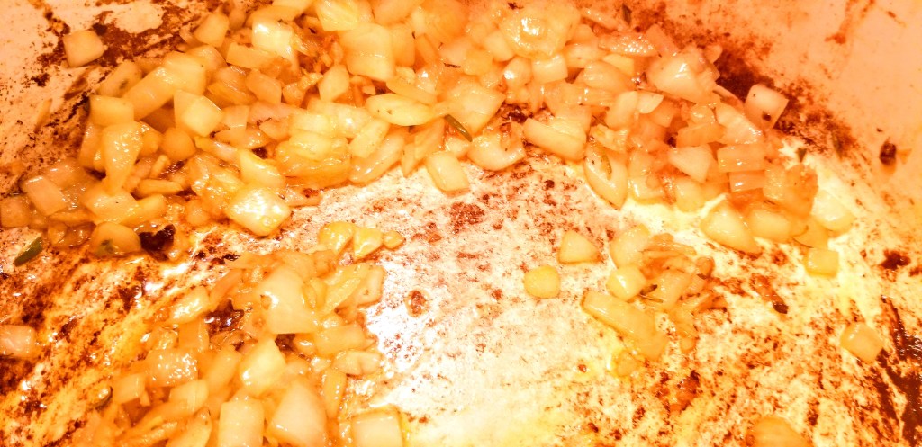 A photograph of onions frying in a pan with spices.