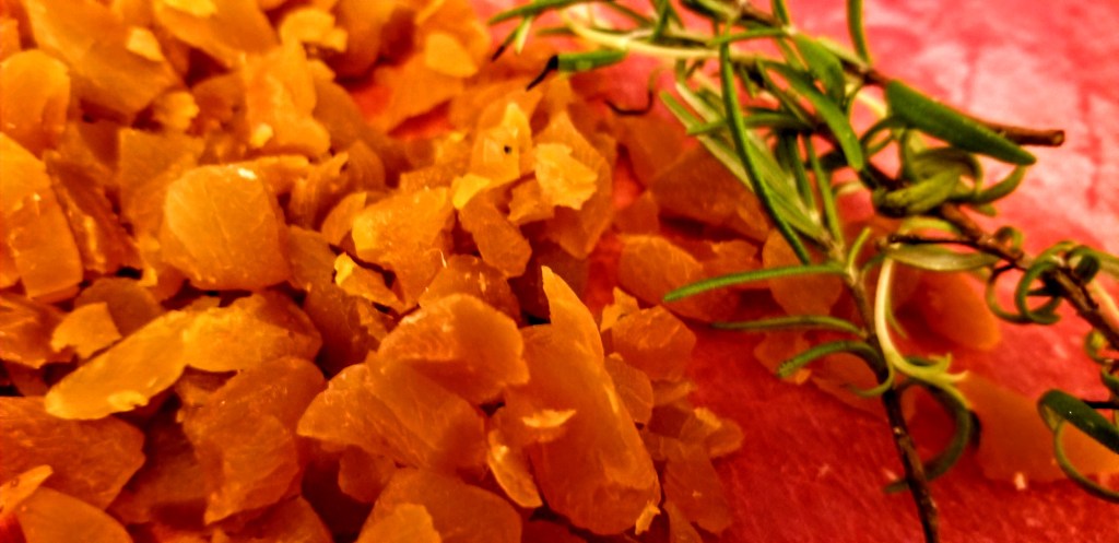 A closeup photograph of chopped apricots and rosemary on a cutting board.