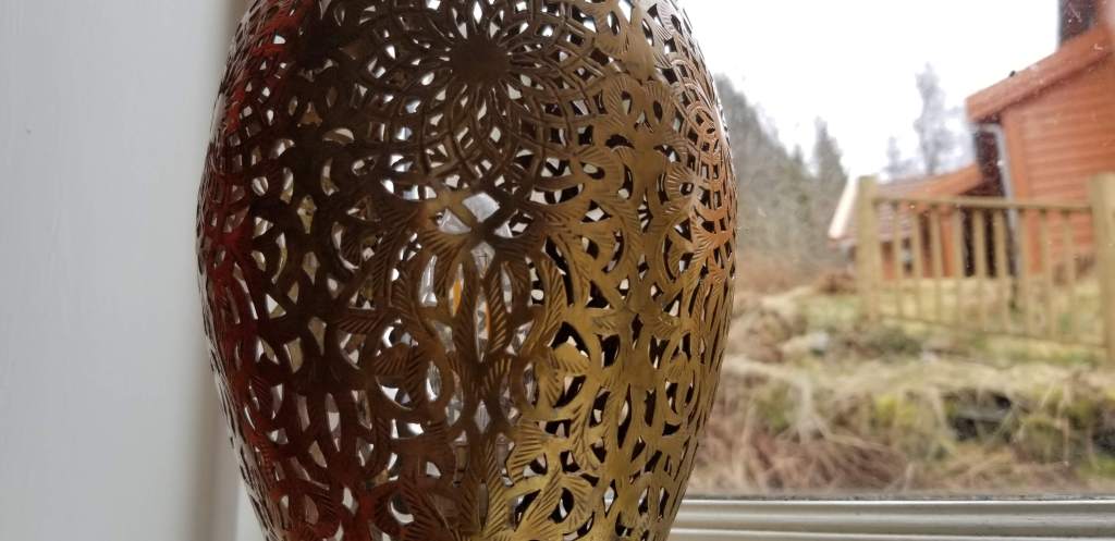 Image of a brass lamp with carved openings in front of a window.