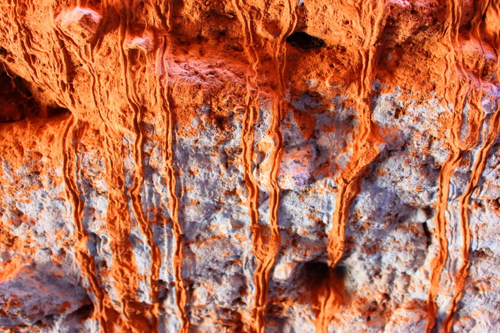 A red earth wall, with rivulets of dried sediment running down over faded blue paint.