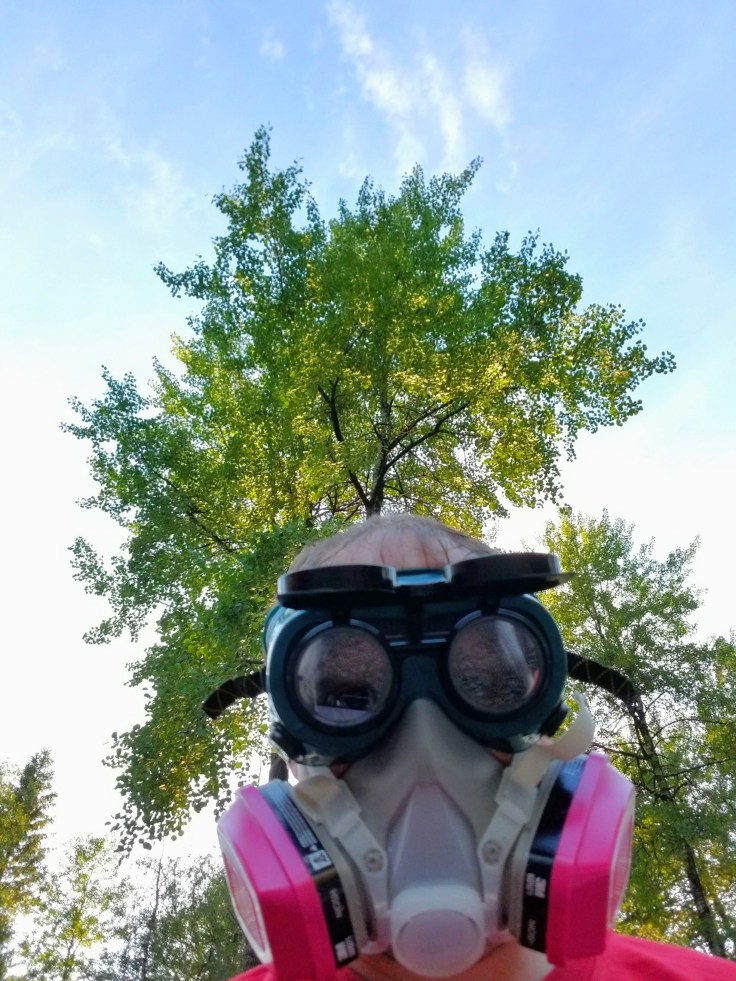 Photograph of a person in ventilator mask and welding goggles in front of a tree.