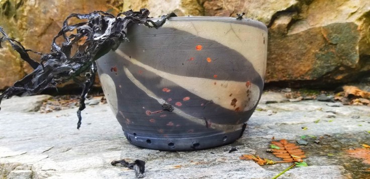 Photograph of a raku ceramic flowerpot with charred paper spilling from its lip.