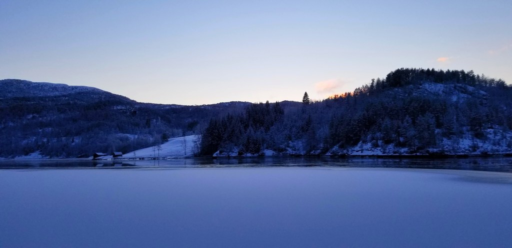 Photograph of a frozen fjord and the land across, at sunset.