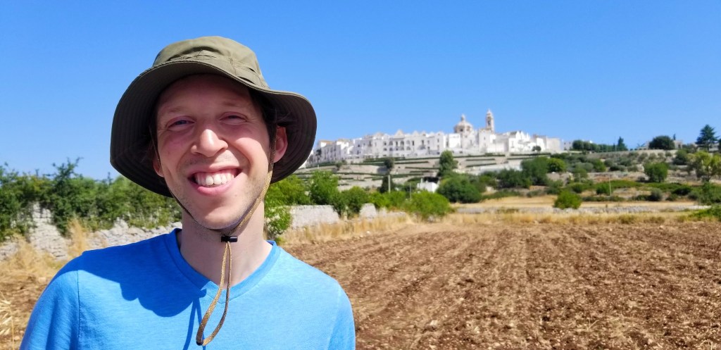 Photograph of the author of this post, Jimmy Kindree, in the countryside in front of the town of Locorotondo.