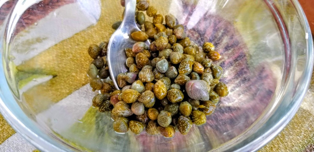 Close-up photograph of capers in a glass bowl.
