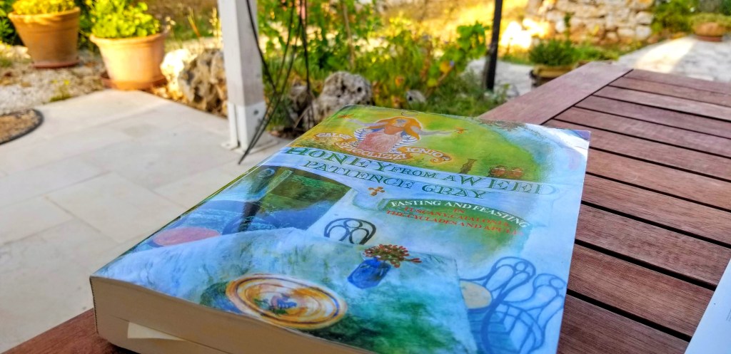 Photograph of the book Honey from a Week by Patience Gray sitting on a wooden table in a garden.
